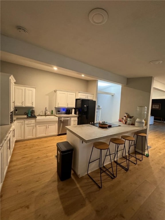 kitchen featuring sink, black refrigerator, light hardwood / wood-style floors, stainless steel dishwasher, and white cabinets