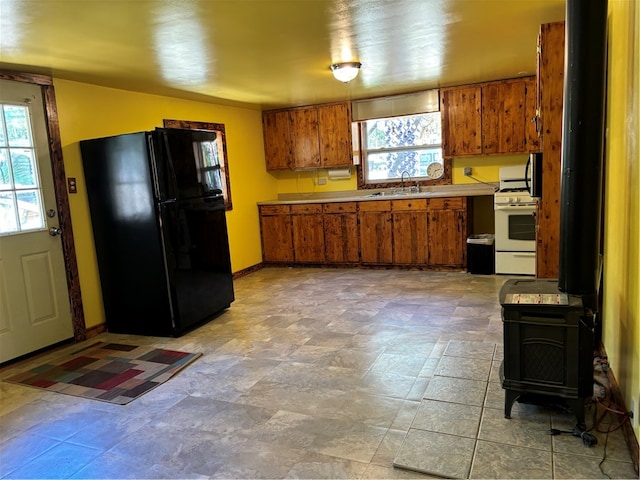 kitchen with a wood stove, a healthy amount of sunlight, white gas stove, and black fridge