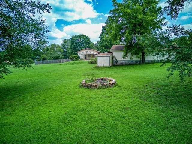 view of yard featuring an outbuilding, an outdoor fire pit, a storage shed, and fence