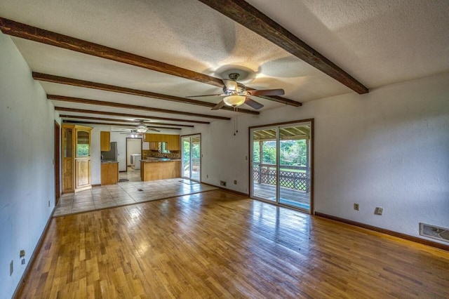 unfurnished living room with beamed ceiling, baseboards, light wood-type flooring, and a textured ceiling