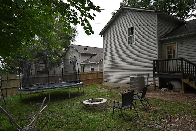 back of house featuring a trampoline, central AC, a fire pit, and a lawn