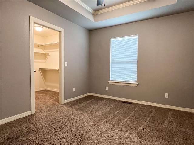 spare room with a tray ceiling, visible vents, dark carpet, ornamental molding, and baseboards