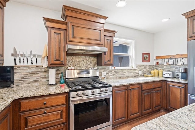 kitchen with backsplash, light stone countertops, under cabinet range hood, and stainless steel appliances