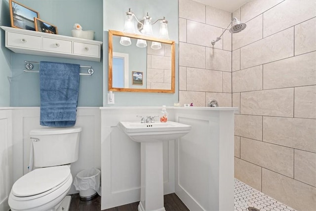 full bathroom featuring wainscoting, toilet, tiled shower, and a sink