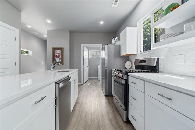 kitchen with appliances with stainless steel finishes, a sink, light countertops, white cabinetry, and backsplash