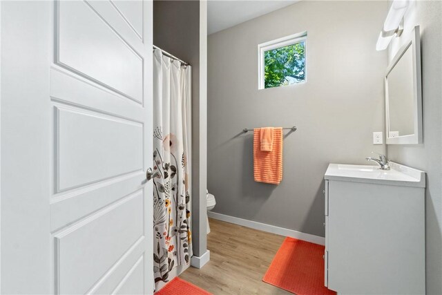 bathroom with a shower with shower curtain, toilet, vanity, wood finished floors, and baseboards