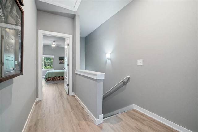 hall featuring light wood-style flooring, baseboards, and an upstairs landing