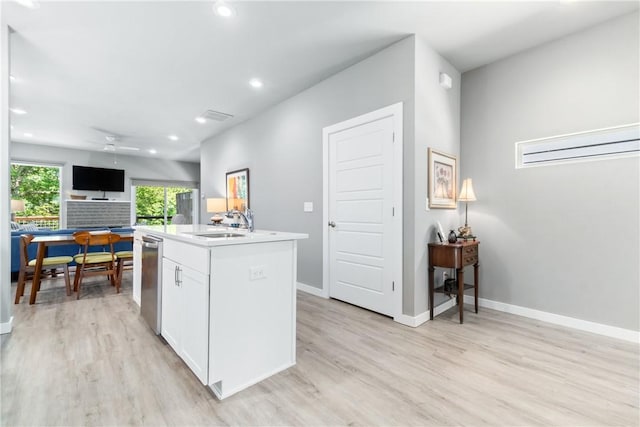 kitchen with light wood-style flooring, a sink, white cabinetry, baseboards, and an island with sink