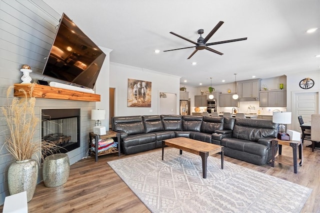 living room featuring ceiling fan, a large fireplace, and wood-type flooring