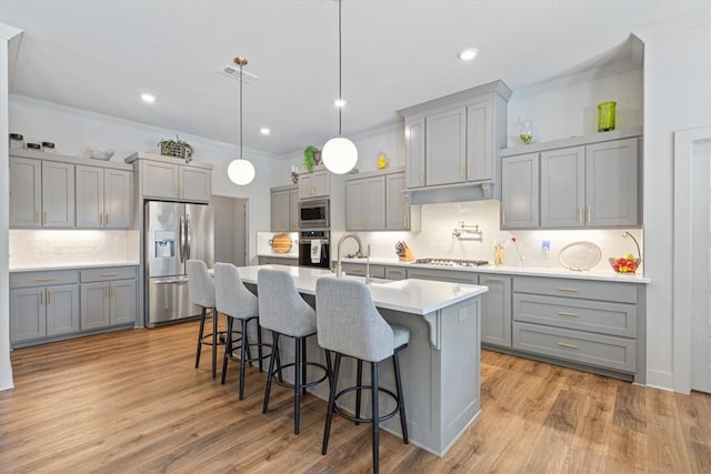 kitchen featuring light wood-type flooring, backsplash, a center island with sink, and appliances with stainless steel finishes