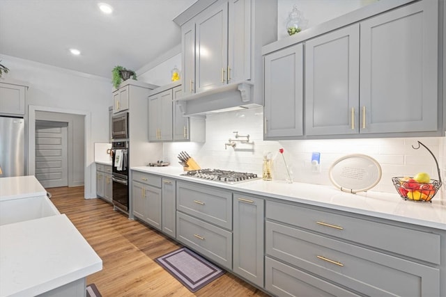 kitchen with backsplash, stainless steel appliances, light hardwood / wood-style flooring, ornamental molding, and gray cabinets