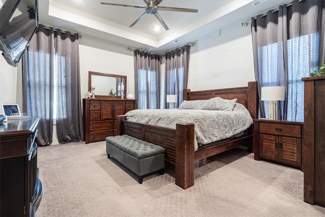 bedroom with a raised ceiling, light colored carpet, and multiple windows