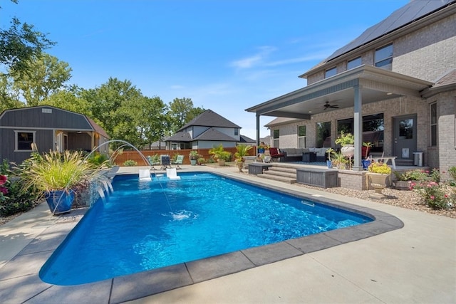 view of swimming pool with a patio, an outdoor structure, pool water feature, ceiling fan, and an outdoor living space