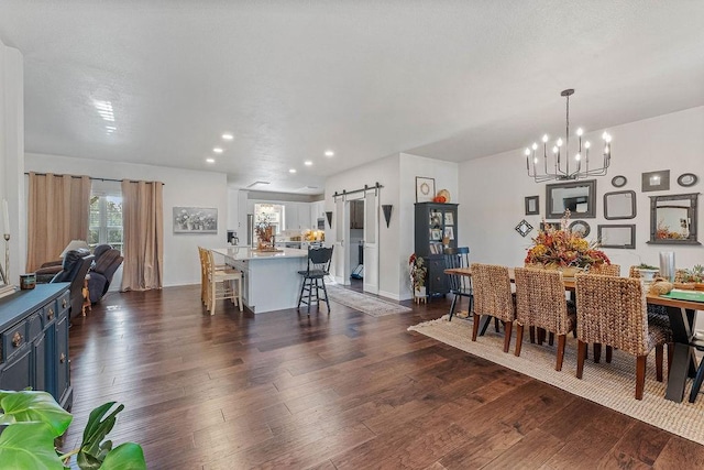 dining room with a barn door, an inviting chandelier, and dark hardwood / wood-style flooring