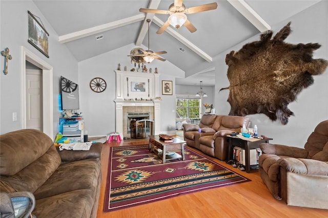 living room featuring visible vents, a tile fireplace, lofted ceiling with beams, wood finished floors, and ceiling fan with notable chandelier