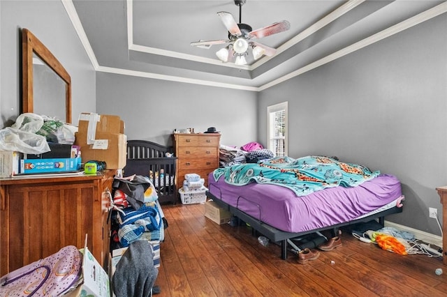 bedroom featuring ceiling fan, hardwood / wood-style floors, baseboards, a tray ceiling, and crown molding