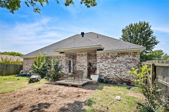 rear view of house with a shingled roof, a lawn, fence private yard, a deck, and brick siding