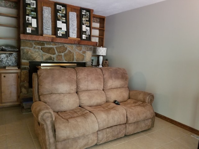 tiled living room featuring baseboards and a stone fireplace