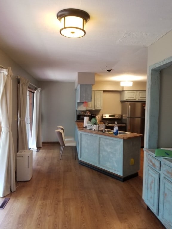 kitchen featuring a peninsula, visible vents, wood finished floors, and freestanding refrigerator