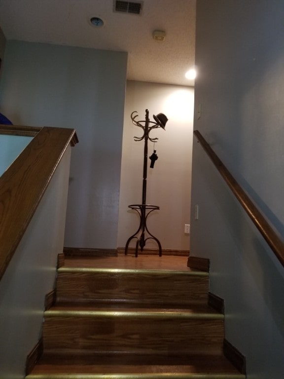 staircase with wood finished floors, visible vents, and baseboards