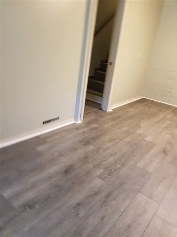 empty room with stairway, baseboards, visible vents, and wood finished floors