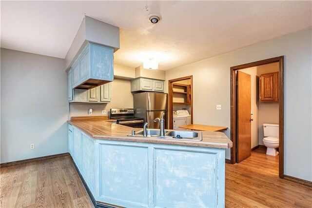 kitchen featuring appliances with stainless steel finishes, a peninsula, washer and dryer, light wood-style floors, and a sink