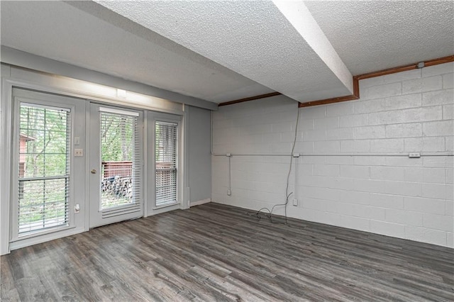 unfurnished room featuring dark wood-type flooring, concrete block wall, and a healthy amount of sunlight