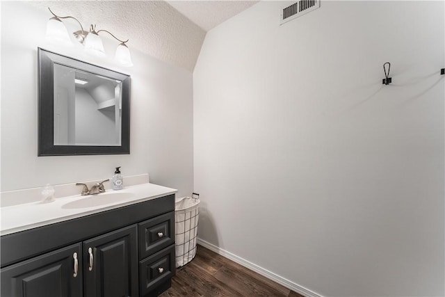 bathroom featuring visible vents, baseboards, vanity, wood finished floors, and a textured ceiling