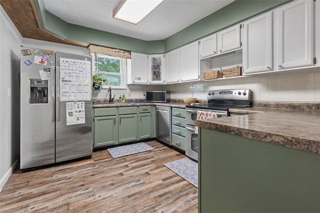 kitchen with appliances with stainless steel finishes, decorative backsplash, light hardwood / wood-style floors, a textured ceiling, and white cabinetry