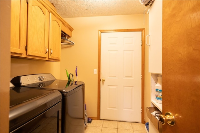 clothes washing area featuring light tile patterned flooring, washing machine and clothes dryer, a textured ceiling, and cabinets