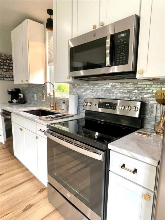 kitchen featuring light wood-style flooring, a sink, white cabinetry, appliances with stainless steel finishes, and tasteful backsplash