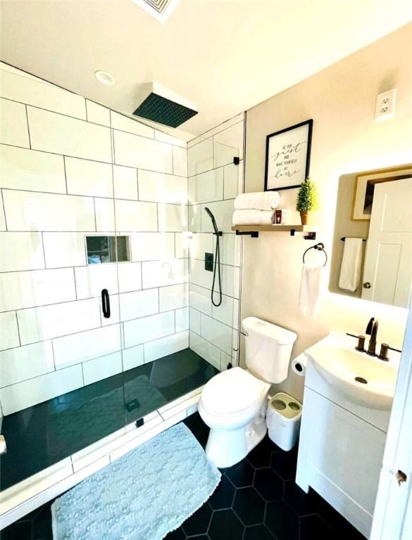 full bathroom with tile patterned flooring, a tile shower, vanity, and toilet