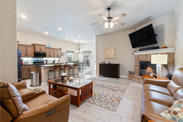 living room featuring ceiling fan with notable chandelier and a brick fireplace