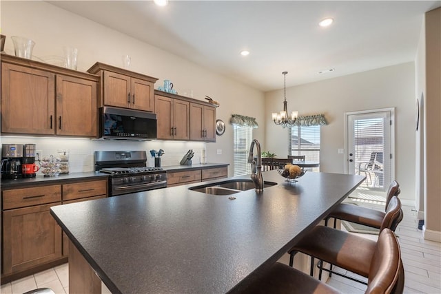 kitchen featuring sink, an inviting chandelier, stainless steel gas range, backsplash, and an island with sink