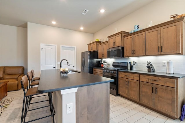 kitchen with gas stove, sink, refrigerator with ice dispenser, a breakfast bar area, and a kitchen island with sink