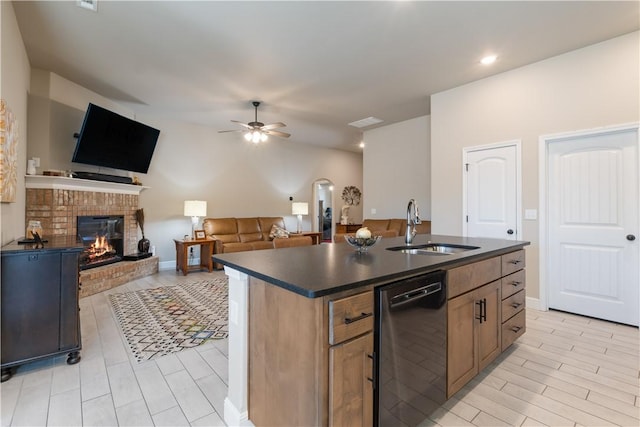 kitchen with ceiling fan, sink, stainless steel dishwasher, a fireplace, and a center island with sink