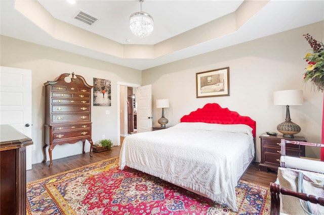 bedroom featuring a raised ceiling, dark wood-type flooring, and a chandelier