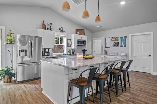 kitchen featuring stainless steel appliances, light hardwood / wood-style floors, decorative light fixtures, white cabinets, and a center island