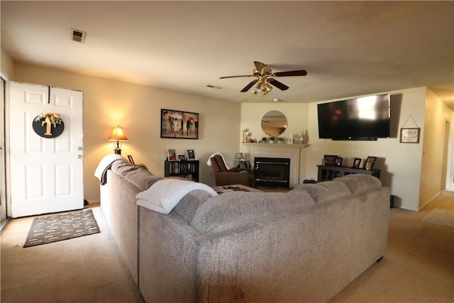 living room featuring a ceiling fan, a glass covered fireplace, visible vents, and carpet