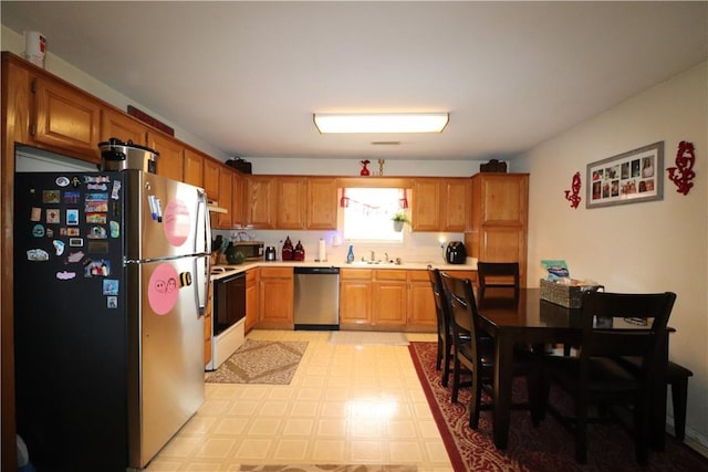 kitchen featuring brown cabinets, light floors, light countertops, appliances with stainless steel finishes, and a sink