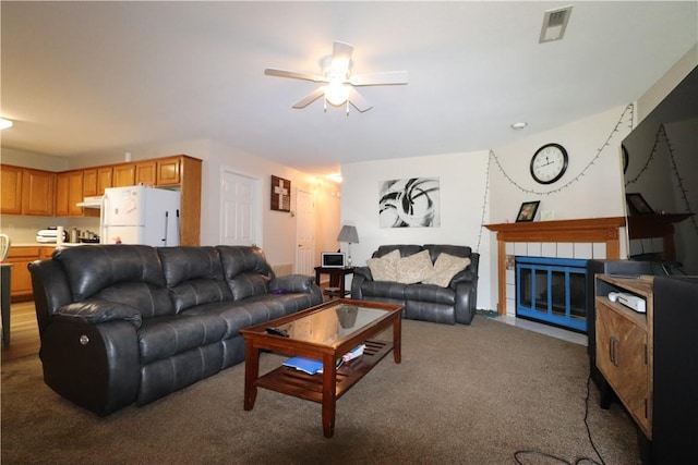 living room featuring ceiling fan, carpet, a tile fireplace, and visible vents