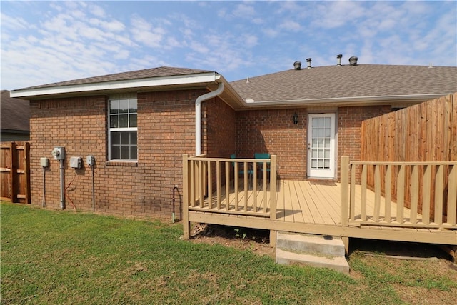 rear view of house with a lawn, roof with shingles, fence, a deck, and brick siding