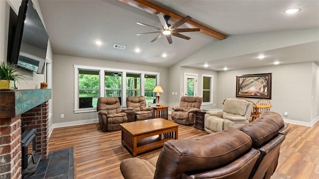 living room featuring vaulted ceiling with beams, light wood-type flooring, visible vents, and a brick fireplace