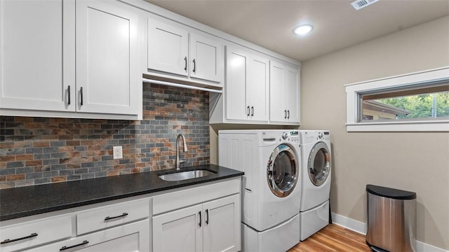 laundry area featuring a sink, baseboards, washer and dryer, cabinet space, and light wood finished floors