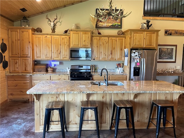 kitchen with appliances with stainless steel finishes, a center island with sink, light stone countertops, a kitchen breakfast bar, and vaulted ceiling