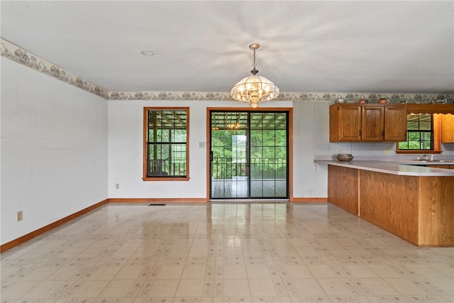 kitchen featuring an inviting chandelier, kitchen peninsula, light tile patterned flooring, pendant lighting, and a textured ceiling