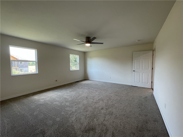 empty room with dark carpet, ceiling fan, and a wealth of natural light