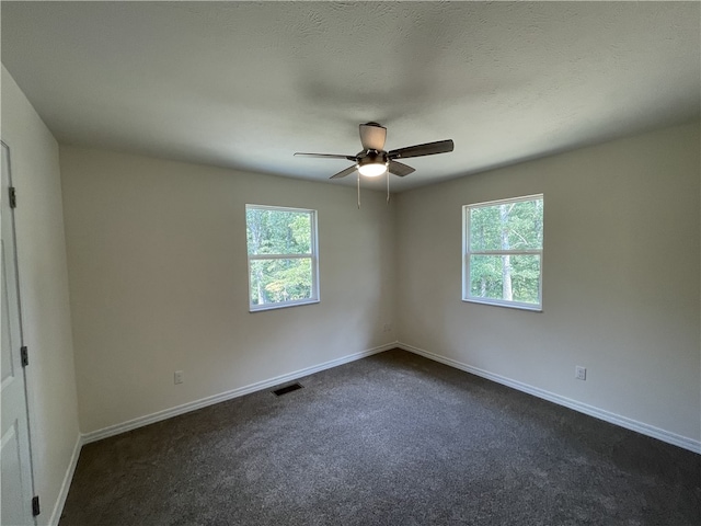 empty room featuring dark colored carpet, ceiling fan, and a healthy amount of sunlight