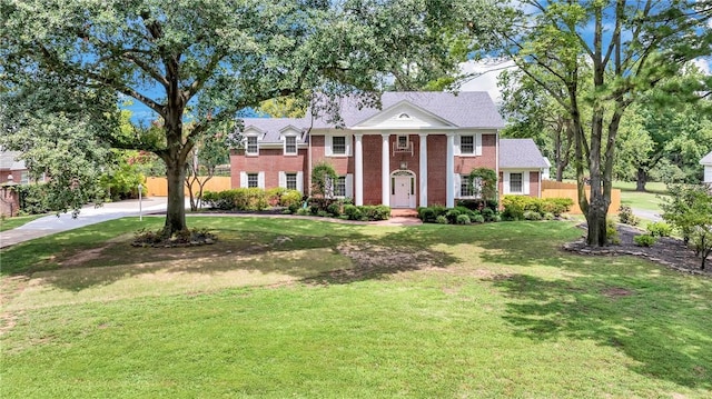 greek revival house featuring a front yard, fence, and brick siding