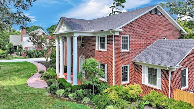 view of property exterior featuring brick siding, a lawn, a shingled roof, and fence